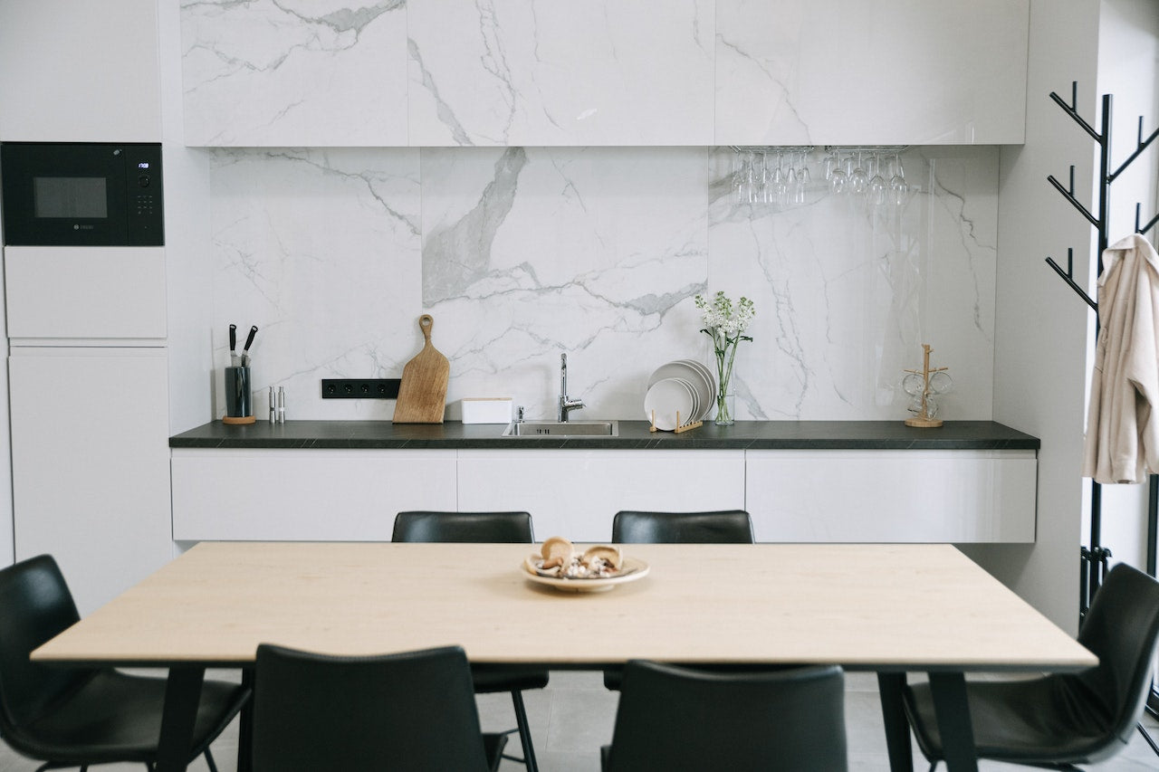 Minimalist kitchen and dining area, with concealed storage, white backdrop on sink, and black dining chairs